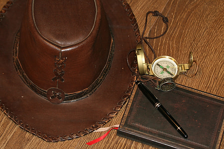 brown leather cowboy hat beside compass on brown wooden surface thumbnail