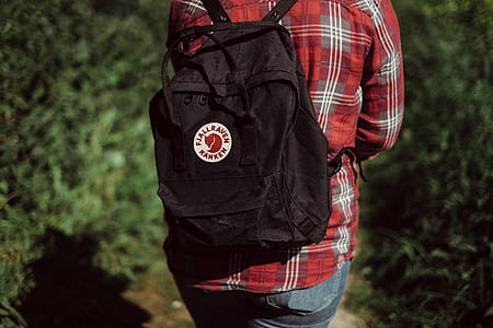 person in red plaid sport shirt with black backpack near bushes thumbnail