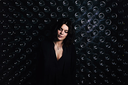 Image of a woman standing by a wall containing glass bottles thumbnail