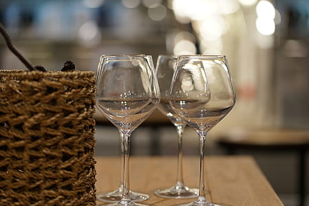 focus photo of four clear long-stemmed wine glasses beside brown basket on brown surface thumbnail