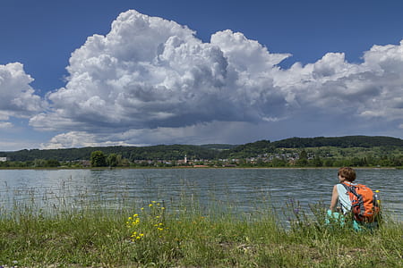 man sitting wearing backpack beside body of water thumbnail