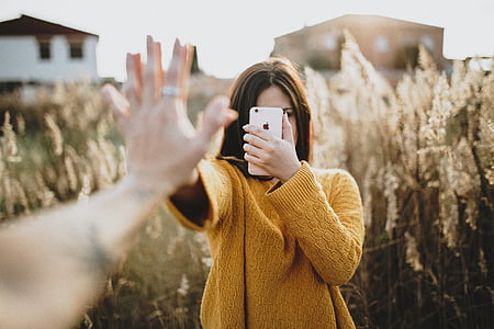 selective focus photo of woman holding iPhone near brown leafed plant thumbnail