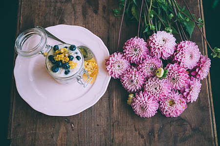 pink petaled flower beside plate on brown wooden surface thumbnail