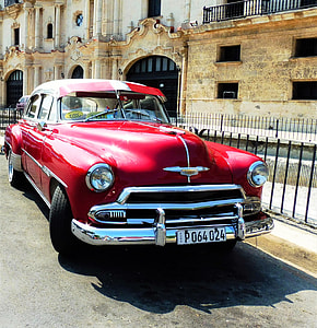 classic red sedan parked on roadside near black fence thumbnail