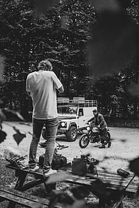 grayscale photo of man standing on picnic table thumbnail