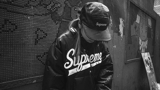 grayscale photography woman in Supreme leather jacket leaning against wall thumbnail