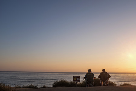 two person sitting on camping chairs facing body of water during golden hour thumbnail