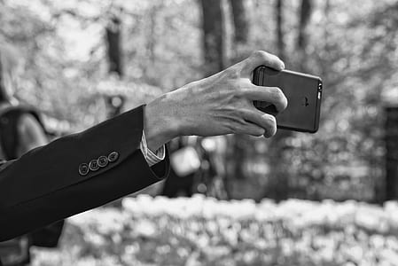 grayscale photo of man's arm holding smartphonje thumbnail