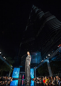 woman standing on stage beside Burj Khalifa at night time thumbnail
