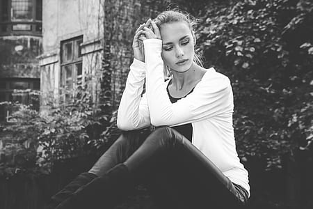 grayscale photo of woman sitting holding her head beside green leafed plant thumbnail