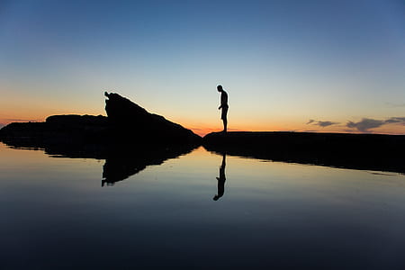 silhouette photo of man standing near body of water during golder hour thumbnail