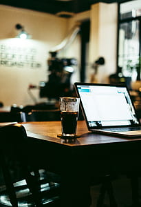 selective focus photography of laptop beside drinking glass on table thumbnail