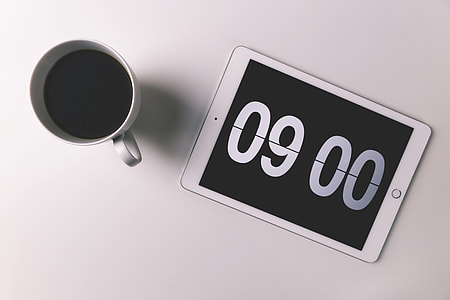 Cup of coffee and iPad with digital clock displaying the morning time thumbnail