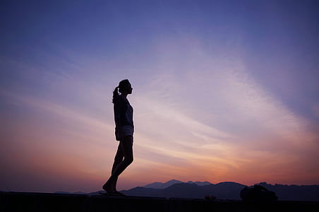 silhouette of woman standing under purple and orange sky thumbnail