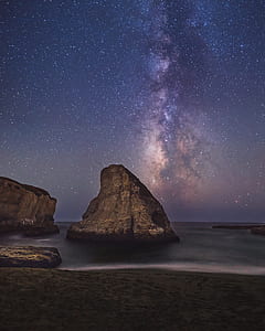 gray rock formation in sea under starry sky thumbnail