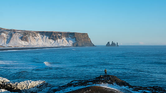 person standing on mound of rock near body of water thumbnail