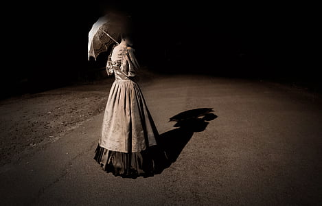 woman in gray dress holding umbrella while standing on concrete floor during nighttime thumbnail