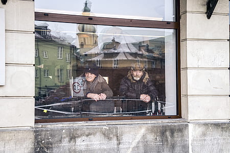two man leaning in front of window thumbnail