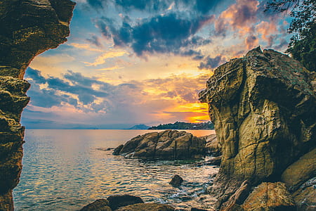 brown rock natural formation beside sea under white clouds thumbnail