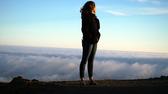 woman standing on hill while while facing white clouds during daytime thumbnail