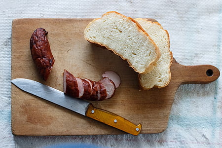 sliced sausage beside bread on brown wooden chopping board thumbnail