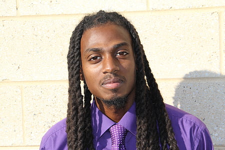 man wearing purple dress shirt leaning on concrete wall thumbnail