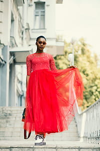 Selective Focus Photo of Woman Wearing Red Floral Long-sleeved Dress Standing on Gray Concrete Pavement thumbnail