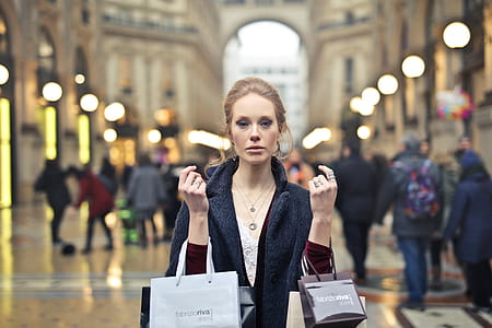 A young blonde woman wearing an overcoat holding shopping bags in her hands thumbnail