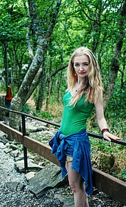 woman wearing green camisole standing behind railing across trees thumbnail