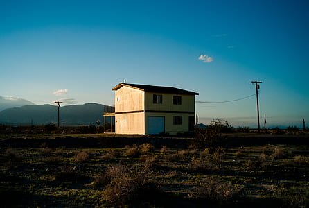 brown 2-storey house on grass field near mountain range under calming clouds thumbnail