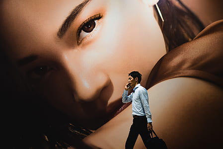 man using smartphone walking beside brown mural thumbnail