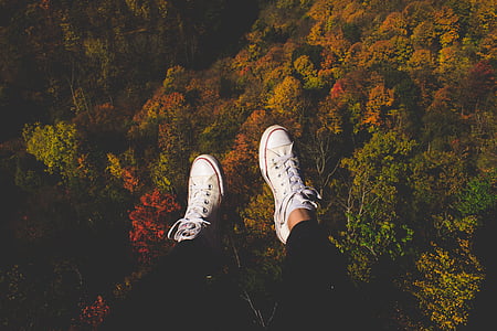 person in black pants sitting at the edge of cliff overlooking trees thumbnail