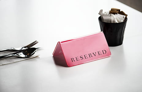 Red Reserved Signage Beside Stainless Steel Spoon and Fork on White Surface thumbnail