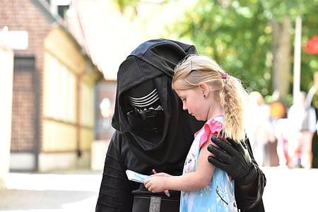 person in black costume besides girl holding notepad thumbnail