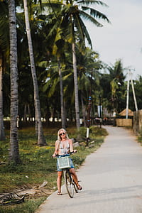 woman riding a bicycle beside green coconut trees thumbnail
