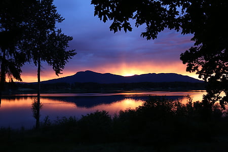 silhouette photography of trees near body of water and mountain thumbnail