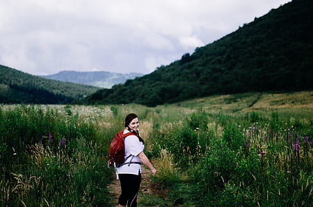 woman walking on pathway surrounded by grass heading towards mountain thumbnail