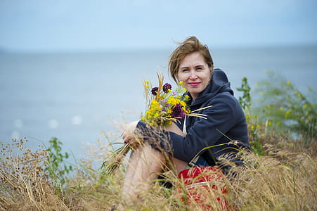 Woman Sitting on Grass Holding Flowers Wearing Black Hoodie thumbnail