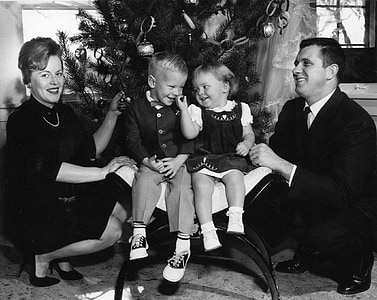grayscale photo of man, woman, and two toddlers sitting near Christmas tree inside room thumbnail