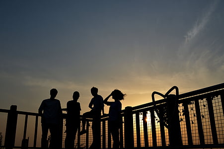silhouette of four people beside fence during sunset thumbnail