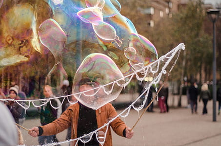 man in brown jacket creating bubbles on park during daytime thumbnail