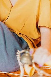 woman wearing yellow top and gray bottoms holding telephone thumbnail