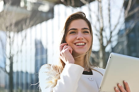 Young Woman In White Jacket Smiling While Using Smartphone And Tablet As Walking on the Road thumbnail