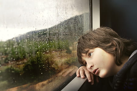 boy resting cheek on hand while looking outside window thumbnail
