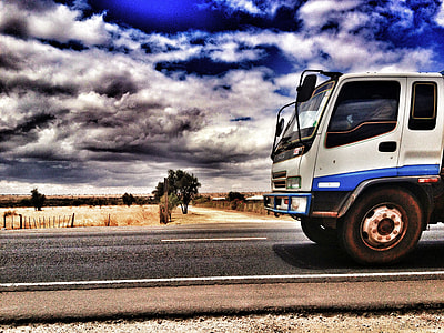 photo of a white and blue truck on the road near wheat fields during daytime thumbnail