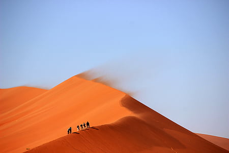 people walking on sand dune under clear blue sky thumbnail