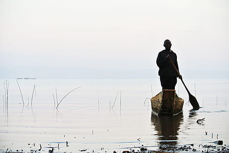 man standing on row boat paddling near shore during daytime thumbnail