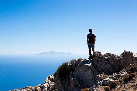 man standing on rock overlooking island thumbnail