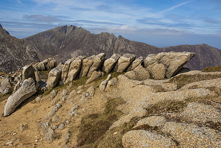 brown rocks on top of mountain under blue and white cloudy sky thumbnail