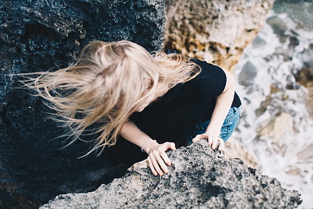woman climbing on rock formation taken at daytime thumbnail
